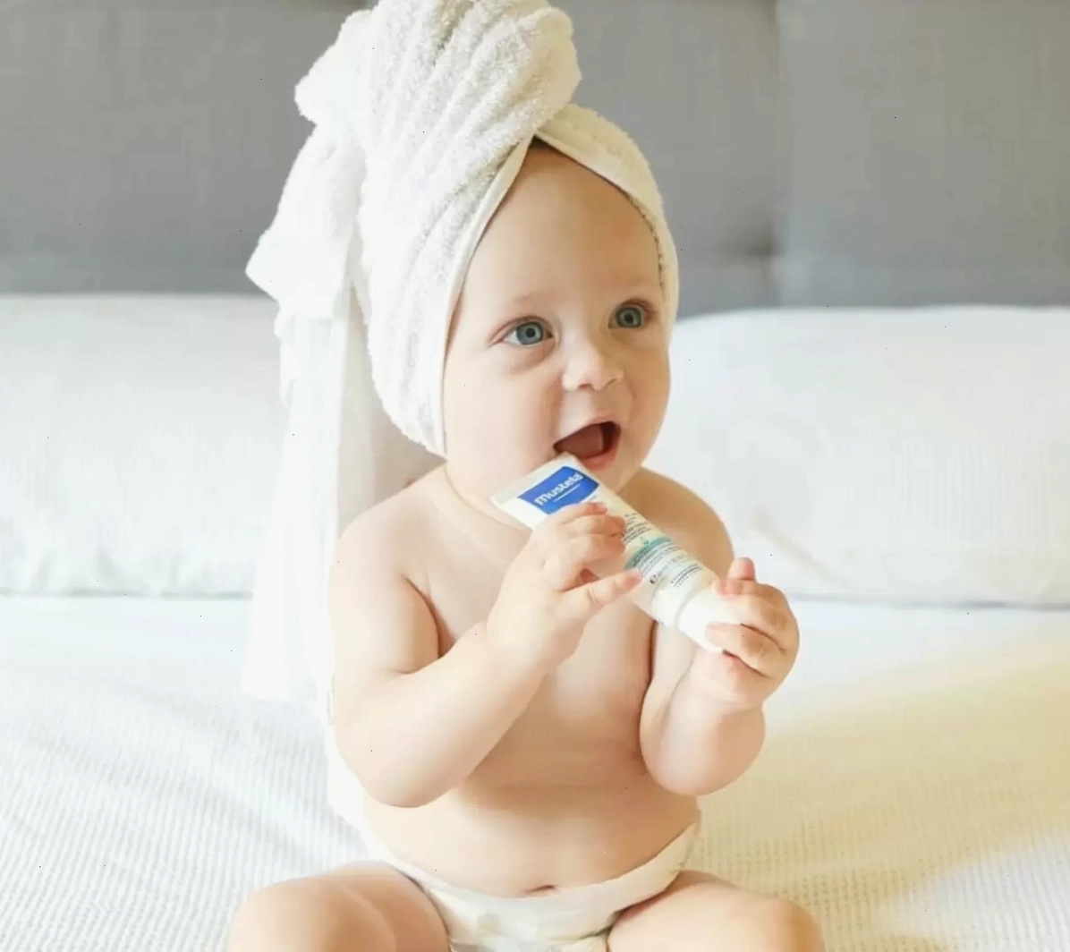 Bé đang ngồi trên bồn tắm với khăn choàng đầu, tay cầm một chai dầu gội tốt nhất cho bé